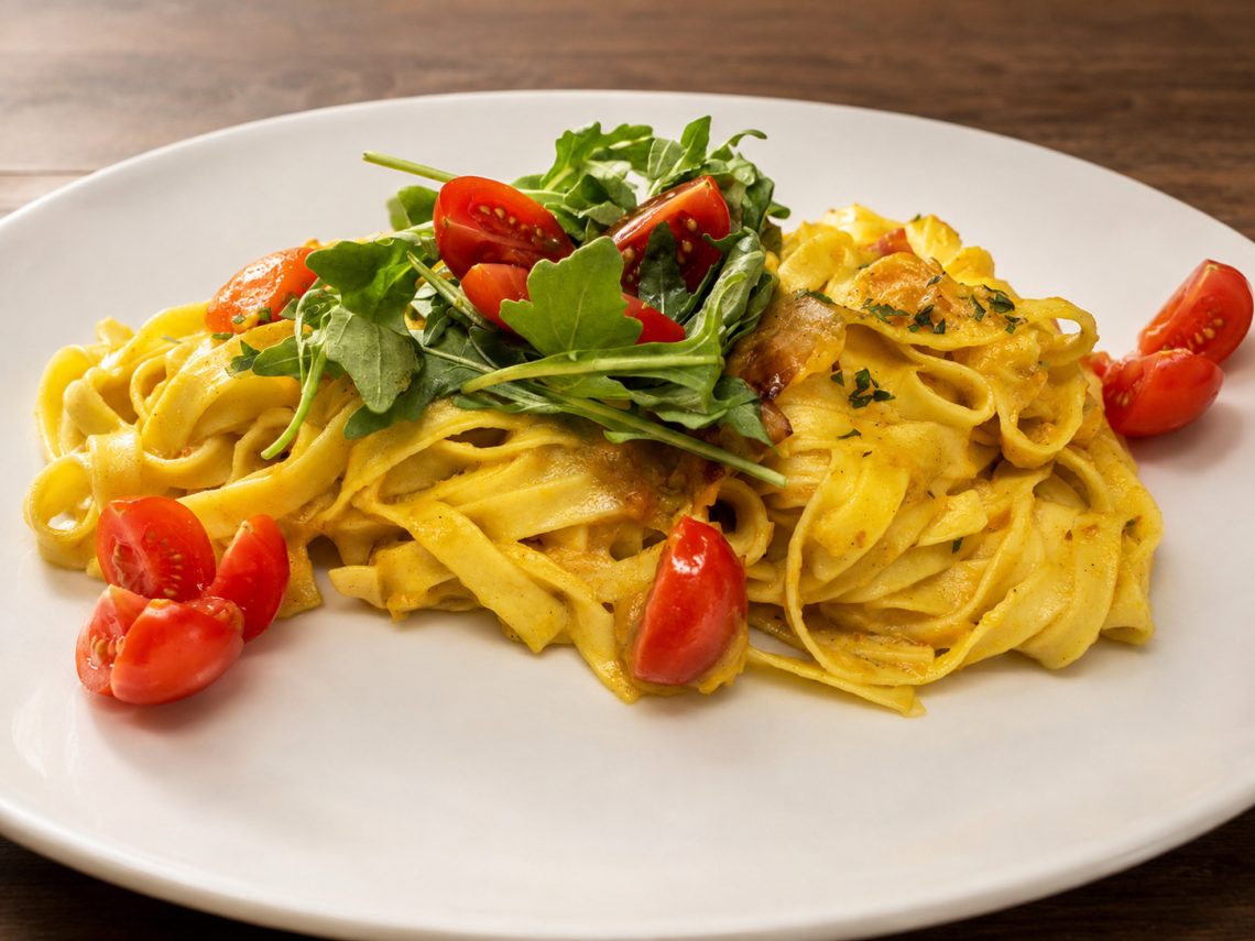 Gelbe Bandnudeln mit Rucola und roten Kirschtomaten auf einem Restaurantteller