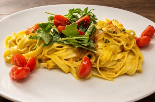 Gelbe Bandnudeln mit Rucola und roten Kirschtomaten auf einem Restaurantteller