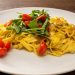 Gelbe Bandnudeln mit Rucola und roten Kirschtomaten auf einem Restaurantteller